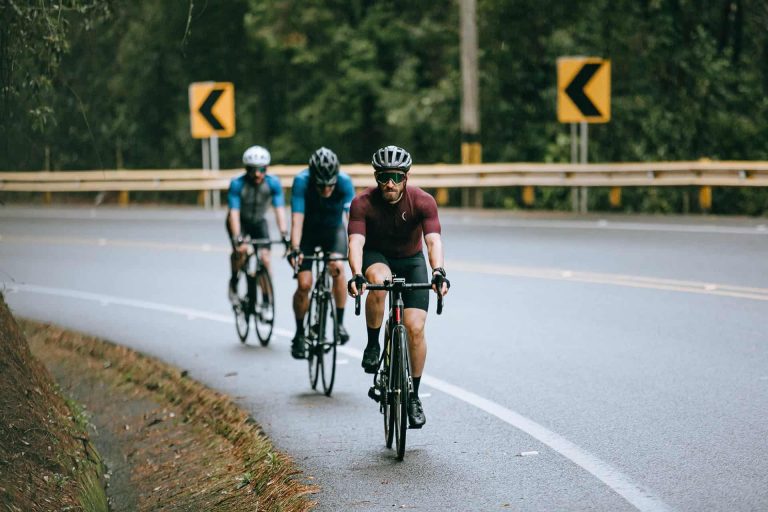 Three cyclists riding on a curved road surrounded by greenery.