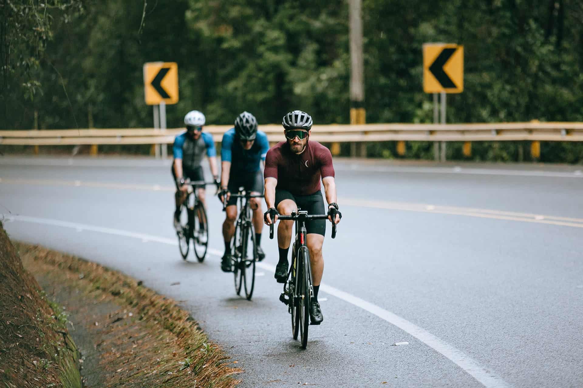 Three cyclists riding on a curved road surrounded by greenery.
