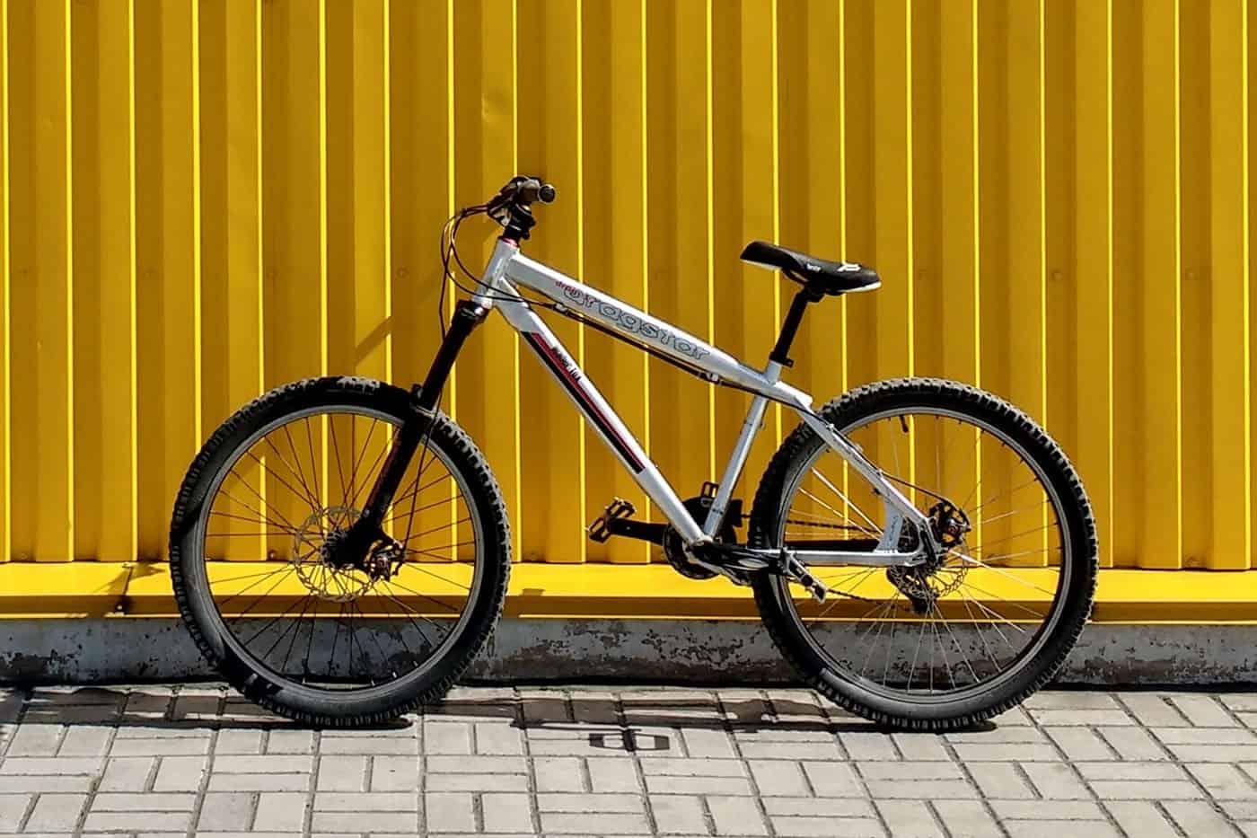A sleek silver mountain bike against a vibrant yellow wall.