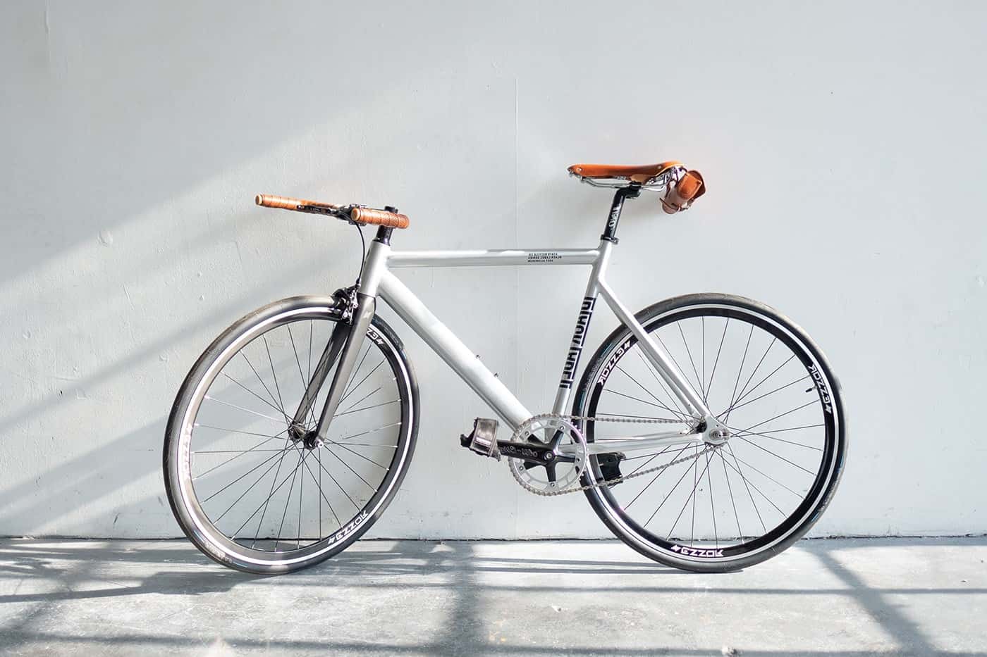 Minimalist white fixed-gear bicycle with brown leather accents.