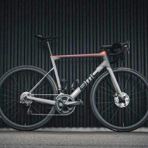 Sleek gray and red road bicycle against a dark corrugated metal background.
