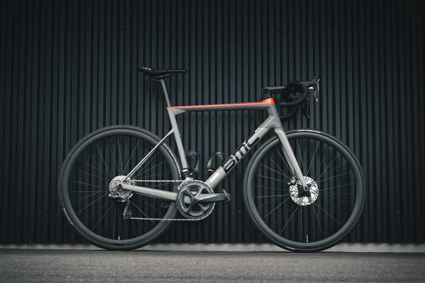 Sleek gray and red road bicycle against a dark corrugated metal background.