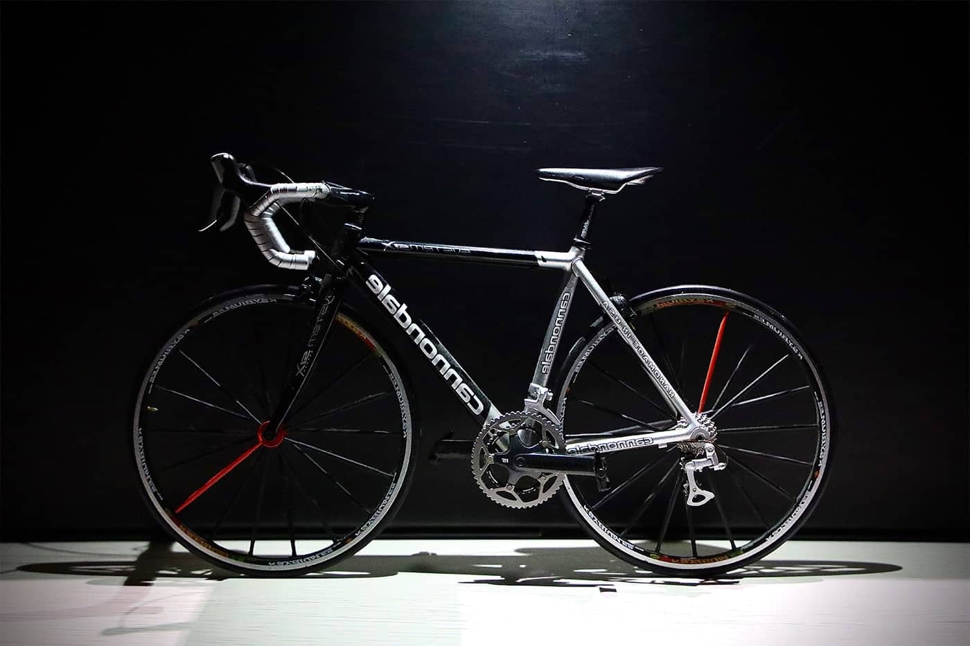 A sleek black and white road bike with drop handlebars against a dark background.