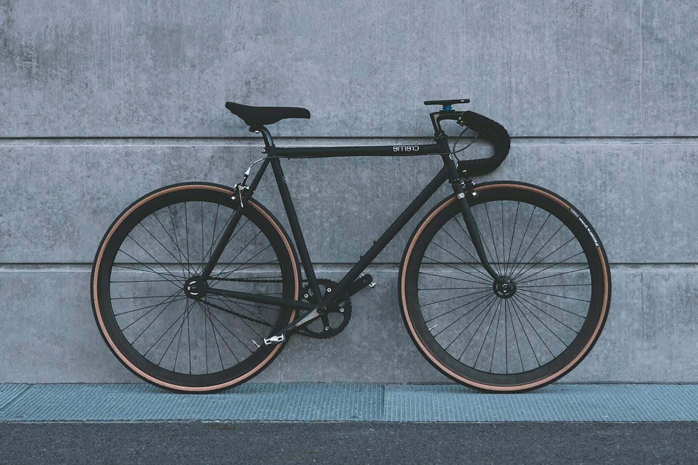 A sleek black road bike against a concrete wall.