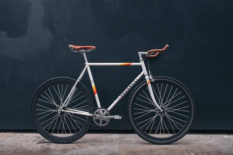 A stylish white fixed-gear bicycle with brown leather handlebars and saddle.