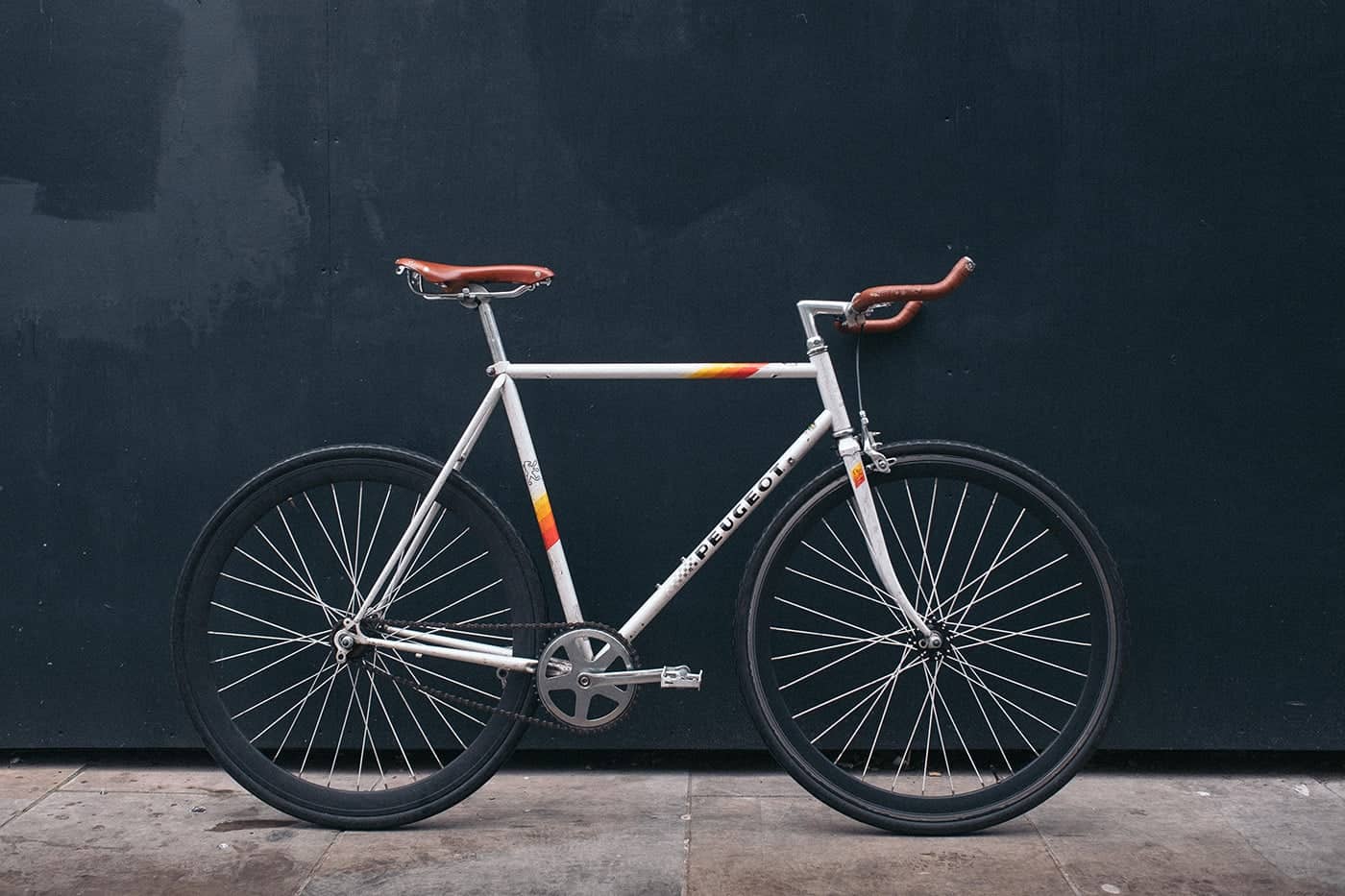 A stylish white fixed-gear bicycle with brown leather handlebars and saddle.