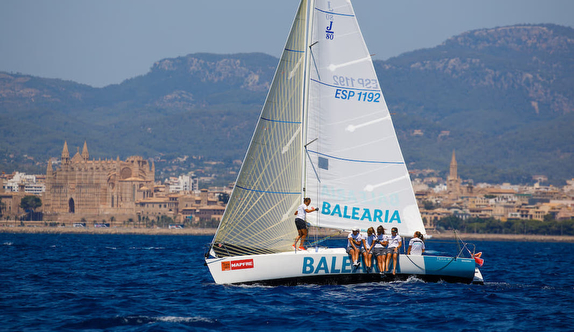 Sailboat with crew near coastal cityscape.