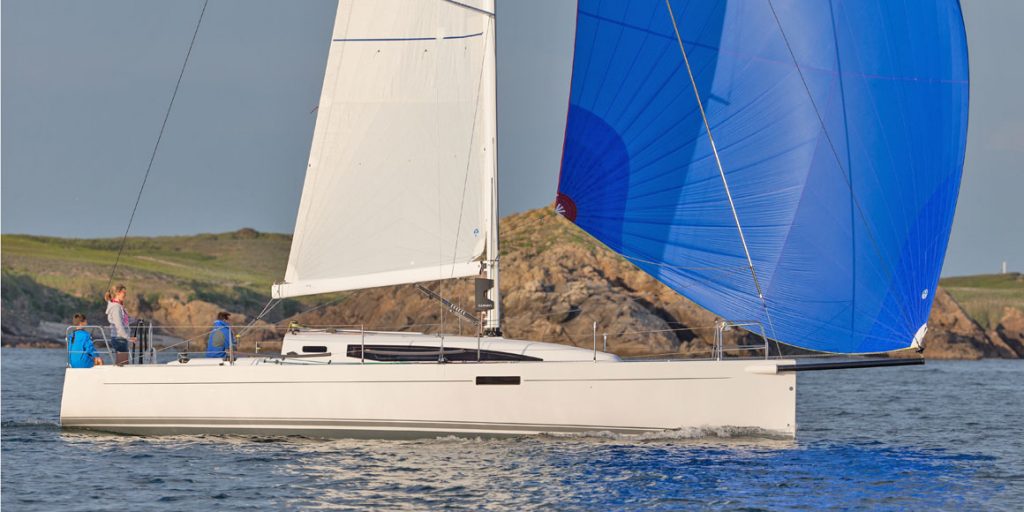 Two sailboats with differently colored sails near a rocky coastline.