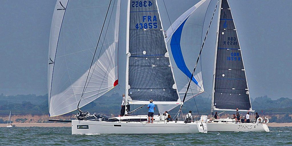 A sailboat gliding on calm water with crew members adjusting sails.