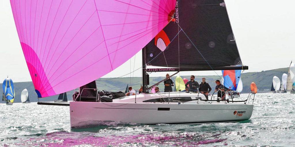 Sailors navigating a boat with a vibrant pink sail on the water.