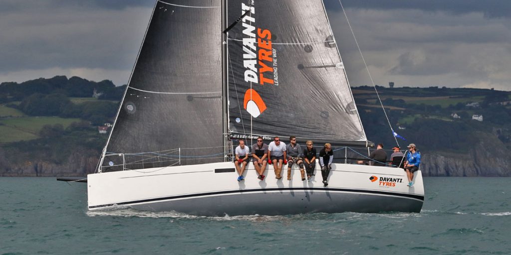 Sailors sitting on the edge of a racing sailboat on calm waters.