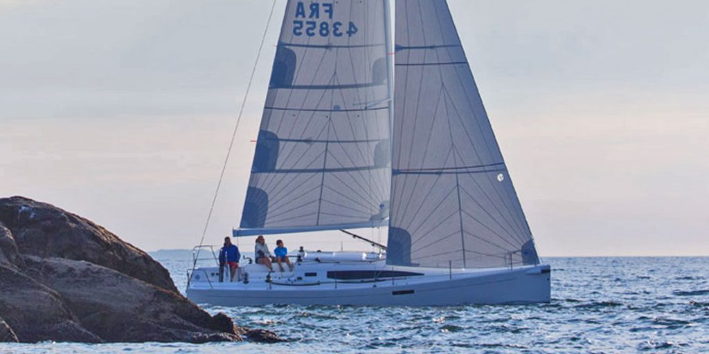 A sailboat glides on the water with its sails fully raised and a crew on board.