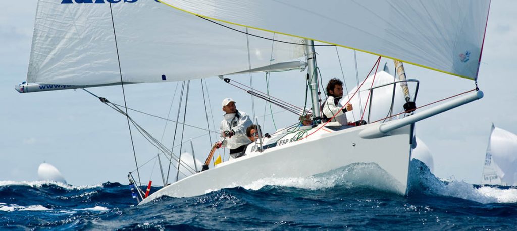 Crew members sail a white yacht on choppy blue waters under a clear sky.