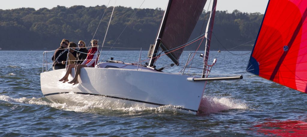 Sailboat gliding on water with a person steering under a clear sky.