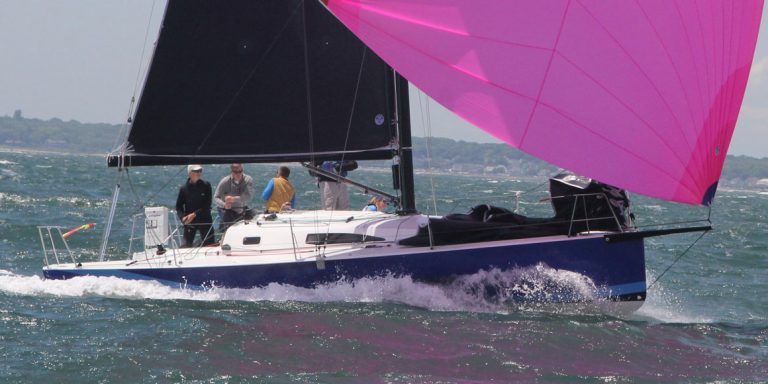Sailboat with a vibrant pink sail gliding through choppy waters.