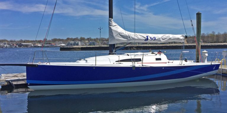 A blue and white sailboat docked in calm water under a clear sky.