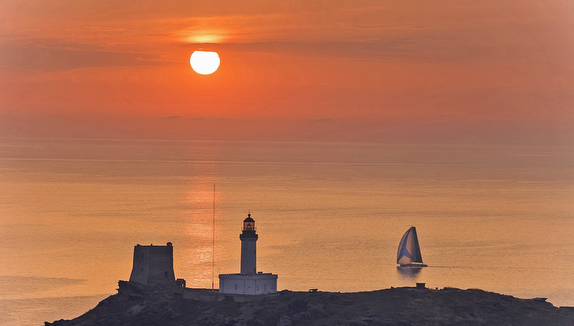 Sunset over lighthouse and sailing boat.