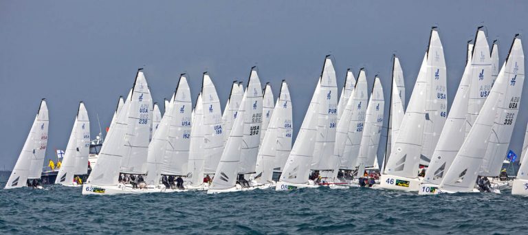 Numerous sailboats racing closely on the water under a clear sky.