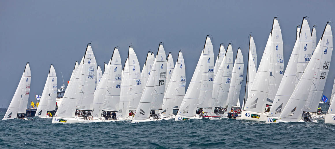 Numerous sailboats racing closely on the water under a clear sky.