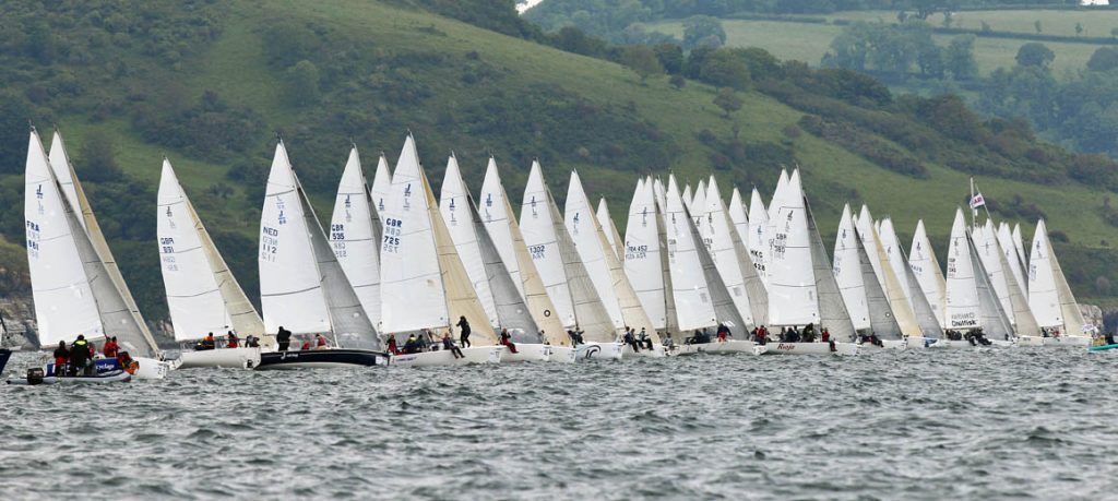 Numerous sailboats lined up on water ready for a race.