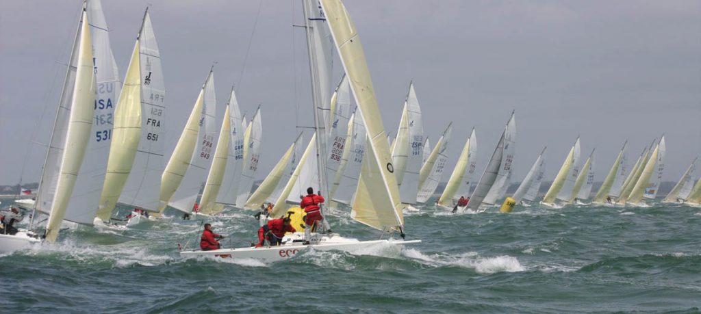 Numerous sailboats racing on choppy waters under cloudy skies.
