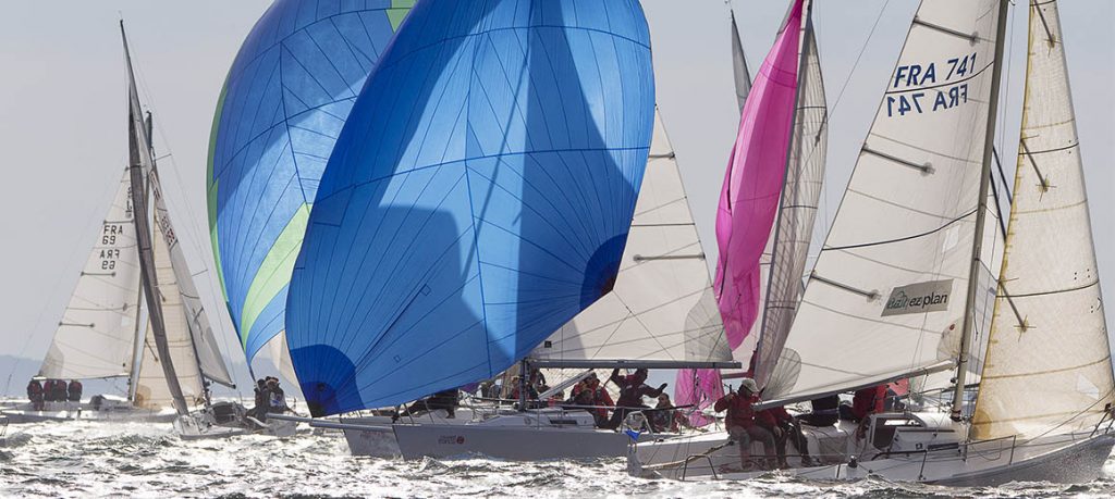 Sailboats racing with vibrant blue and pink sails on the water.