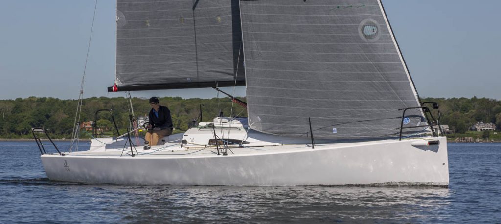 A sleek sailboat with carbon fiber sails glides on calm water, crew onboard.