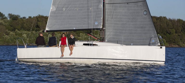 Two women sitting on the edge of a sailboat on calm water.
