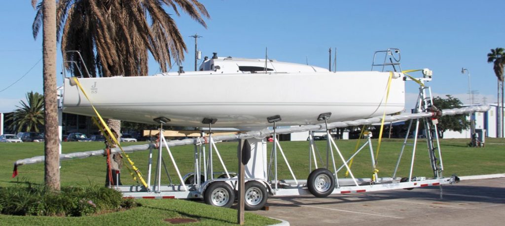 Sailboat hull supported on a trailer with palm trees in the background.