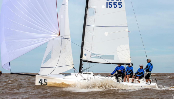 Sailboat racing with team in blue uniforms.
