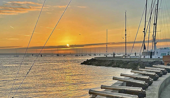 Sunset over harbor with docked sailboats.