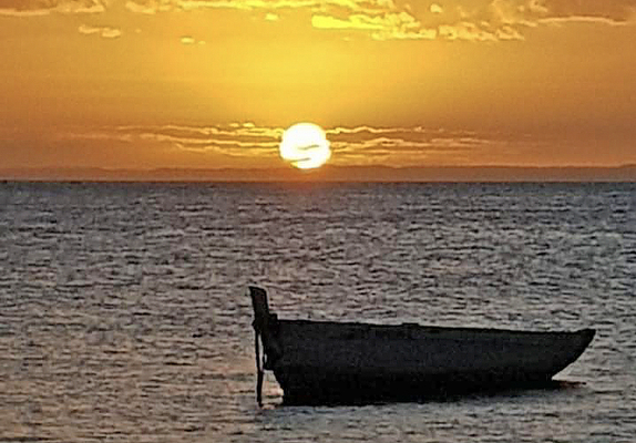 Boat silhouetted against a sunset over water.