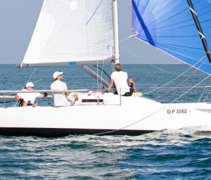 Sailboat with crew navigating calm waters under clear skies.
