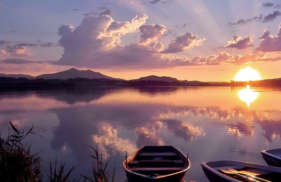 Sunset over lake with boats and mountains.