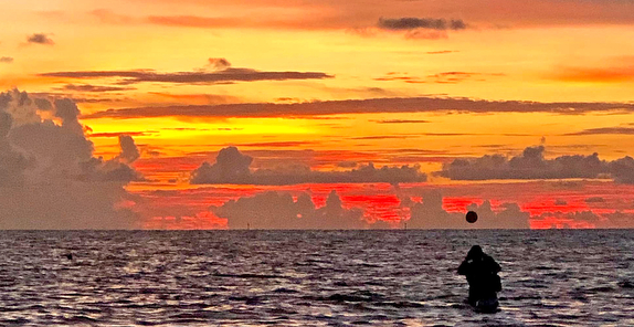 Sunset over ocean with silhouetted figure.