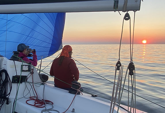 Sailors watching sunset on calm ocean.
