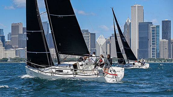 Sailboats racing with city skyline backdrop.