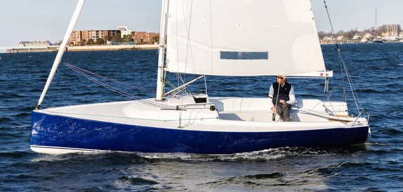 Man sailing small blue sailboat on water.