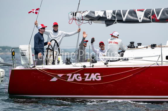 Sailing team aboard a red sailboat named ZIG ZAG during a race.