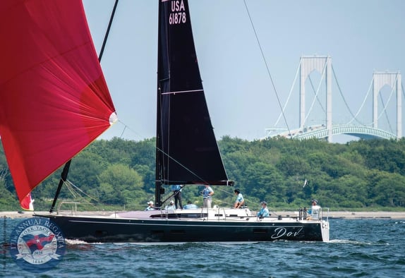 Sailboat with red sail near a bridge.