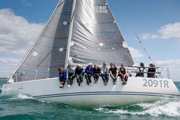 Crew members sit on the edge of a sailboat during a race on the water.