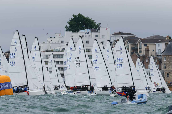 A fleet of sailboats racing on the water under a cloudy sky.