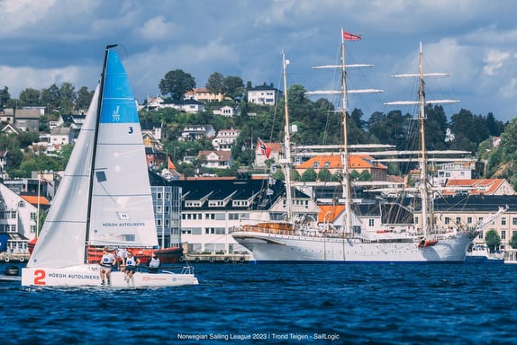 Sailboats and a tall ship near a coastal town with hills in the background.