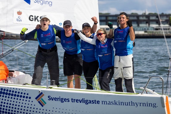 A group of five people celebrating at a sailing event, wearing blue shirts and hats.