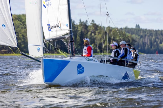 Sailors navigating a blue and white sailboat on a sunny day.