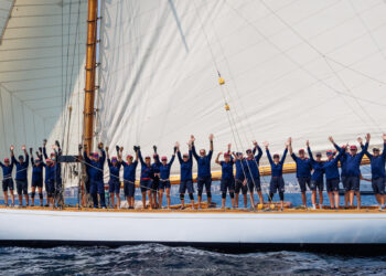 A group of sailors celebrating on a classic sailboat with raised arms.
