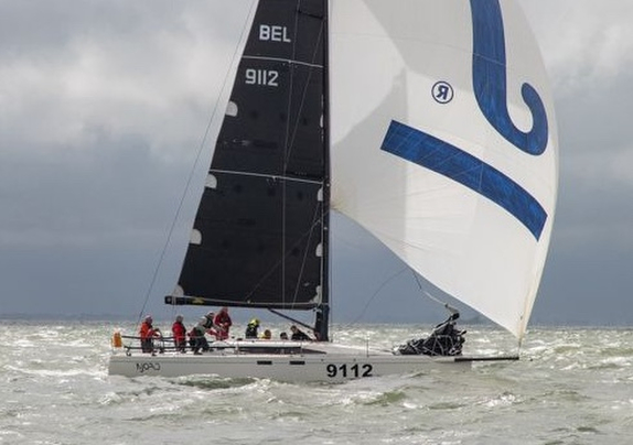 A sailboat with black and white sails racing on choppy water.