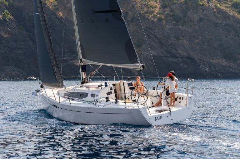 Sailboat with crew navigating near rocky coastline.