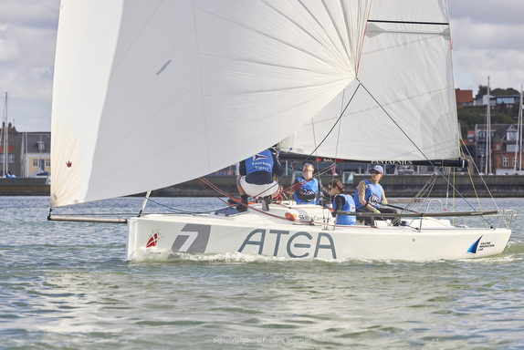 Sailboat with crew racing on calm waters under white sails.