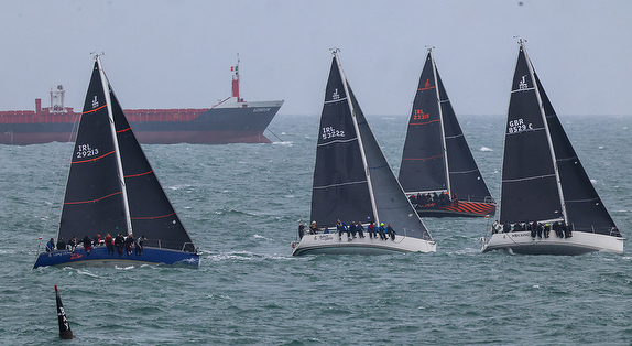 Sailboats racing on a choppy sea with a large cargo ship in the background.